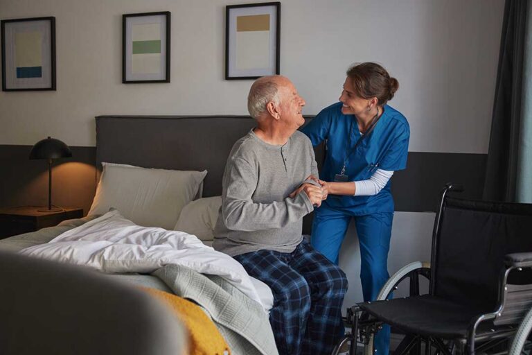 Older adult greeting family members in a bright assisted living lounge while staff manage a visitor sign-in desk.